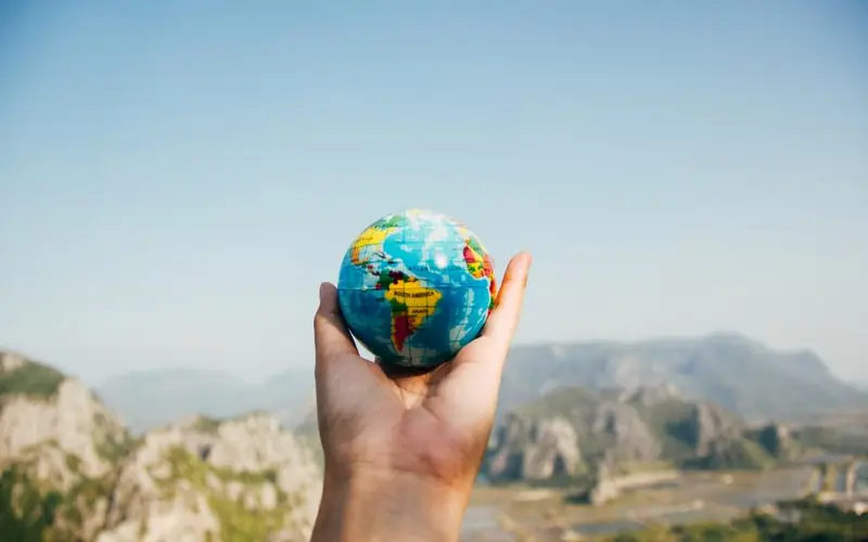 Hand holding a small globe in front of a mountain landscape