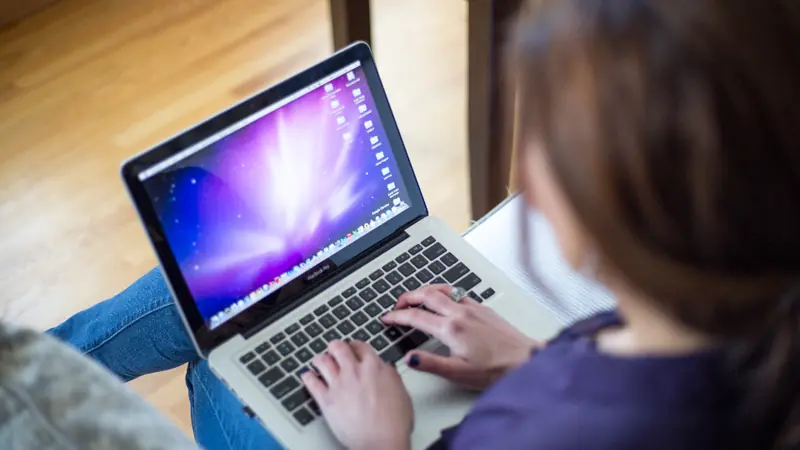 Woman on her sofa typing on a laptop while chatting online