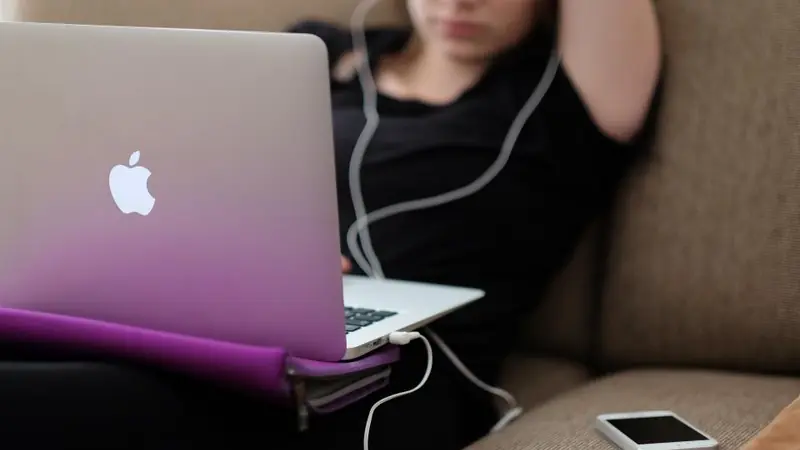 Woman with earphones chatting on her laptop, face hidden behind the screen