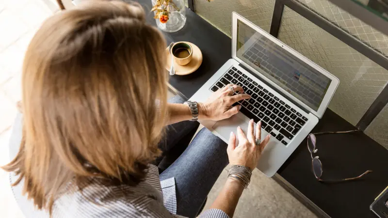Woman typing a chat message on her laptop at a café table
